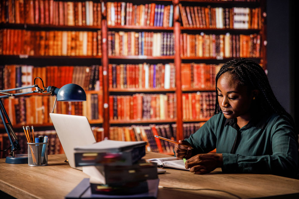 Student studying with books and a laptop in a library.