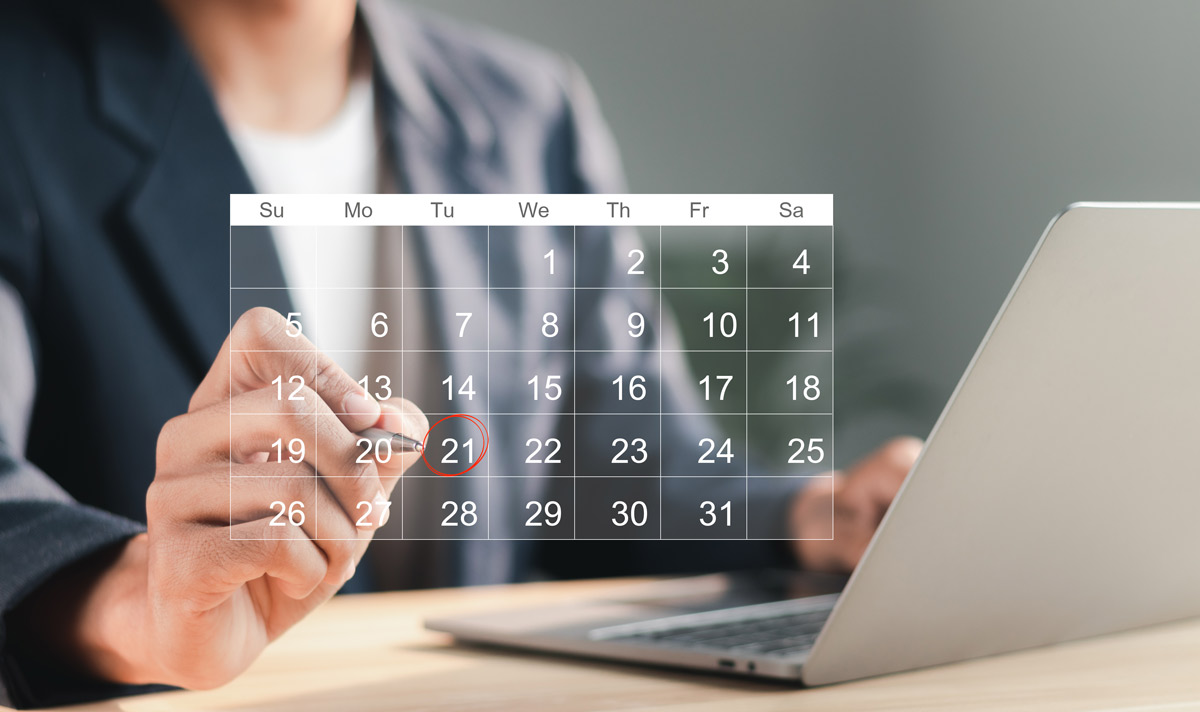 Person marking a calendar date while using a laptop